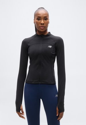 Veste de sport noire à fermeture éclair, en tissu extensible, avec manches longues munies d'ouvertures pour les pouces et un petit logo sur le côté gauche de la poitrine.