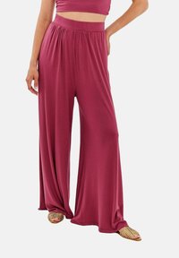 Kalhoty s širokými nohavicemi v růžové barvě, s elastickým pasem a splývavým siluetou. Spárováno se sandály s pásky ve zlaté barvě.