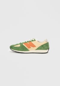 Sneaker cu un brâu din suede verde, accente din piele bej deschis și un logo "N" portocaliu. Prezintă o talpă intermediară albă și o talpă exterioară din cauciuc negru.