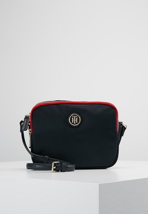 Czarna prostokątna torba na ramię z czerwonym paskiem suwaka, regulowanym paskiem i złotym okrągłym logo na przodzie.