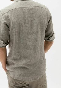 Grau leinene Hemd mit hochgekrempelten Ärmeln, Rückenpasse und entspannter Passform. Die Textur wirkt leicht zerknittert und luftig.