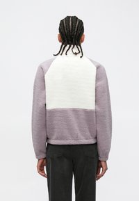 Purple and cream fleece jacket with a high collar, featuring a soft texture and a color-block design. The cuffs are fitted and the hem is straight.