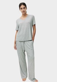 Lys grå loungewear sæt lavet af blødt stof, der består af en top med v-udskæring og korte ærmer samt løstsiddende bukser med snøre og sidelommer.