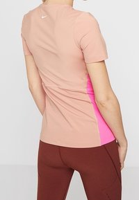 La camiseta deportiva de manga corta de Nike presenta un cuerpo rosa con paneles laterales de un rosa brillante en contraste, fabricada con un material ligero y elástico.