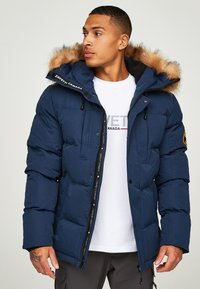 Tumši zils pūšanai paredzēts jakas ar vilnas odere kapuci, ar rāvējslēdzēju un pogu aizdari, kā arī elastīgām aprocēm. Zīmola logo uz krūšu un kreisās rokas.