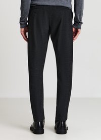 Schwarze maßgeschneiderte Hose aus strukturiertem Stoff mit geradem Bein und dezenten doppelten Gesäßtaschen. Kombiniert mit schwarzen Schuhen.