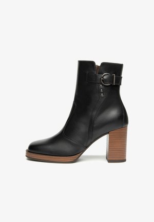 Schwarze Leder-Ankle-Boots mit Holzblockabsatz, seitlichem Schnallenriemen und dekorativen Metallnieten an der Außenseite.