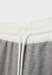 Nahaufnahme von grauen Jogginghosen mit einem weißen elastischen Bund und einem vorne gebundenen weißen Kordelzug.