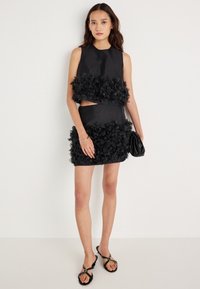 Vestido preto de duas peças com detalhes em aplique floral em camadas. Parte de cima sem mangas com um corte justo, combinada com uma mini saia a condizer.