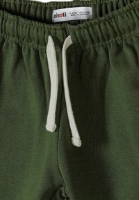 Pantalon de survêtement pour enfants couleur vert olive avec taille élastique, cordons blancs, et une étiquette de taille indiquant 5-6 ans, 110/116 cm, fabriqué au Pakistan.
