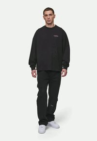 Black long-sleeve sweatshirt with logo detail, paired with black cargo pants featuring pockets and white sneakers for footwear.