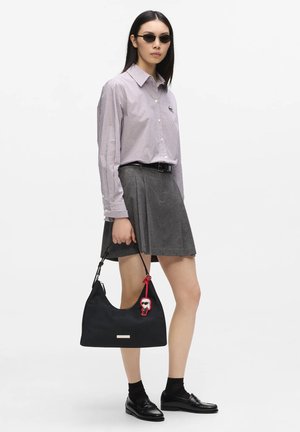 Woman wearing sunglasses, checkered shirt, gray pleated skirt, black loafers, holding a black handbag with a small red keychain.