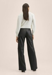 Světle šedý zkrácený svetr s nabíranými rukávy, kombinovaný s černými koženými kalhotami s širokými nohavicemi a vysokým pasem. Hladká textura a minimalistický design.