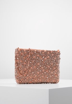 Pochette rectangulaire rose couverte de petits et grands strass transparents avec une fine chaîne, posée sur une surface blanche sur fond uni.