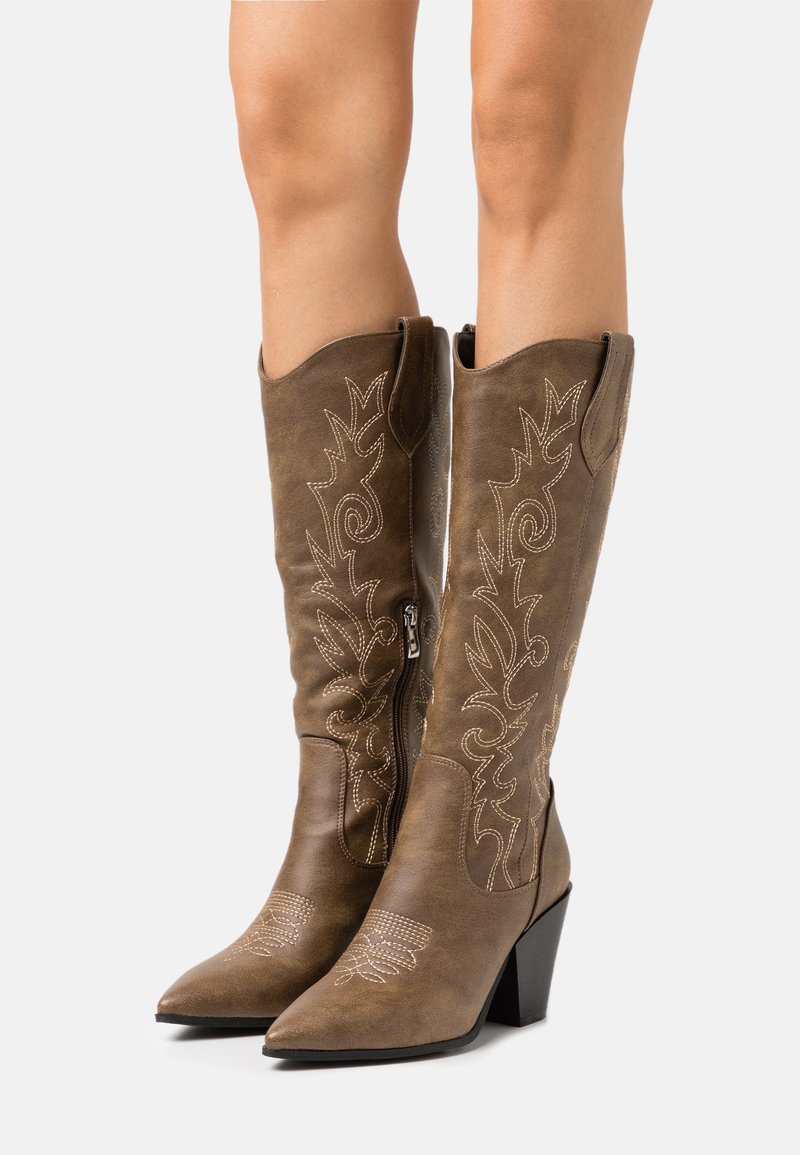Hnědé kožené kovbojské boty s špičatými špičkami a středně vysokými blokovými podpatky. Mají dekorativní bílé prošívání a květinové vzory na holeni.