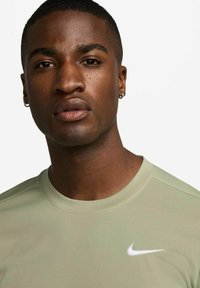 Nike short-sleeve shirt in light green, made of moisture-wicking fabric. Features a white logo on the chest and a classic crew neckline.
