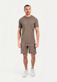 Bruine T-shirt met korte mouwen en bijpassende korte broek, gemaakt van gladde stof, gecombineerd met witte sneakers. Eenvoudig ontwerp, neutraal kleurenpalet.