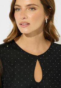 Vestito nero con scollatura rotonda e un'apertura a chiave, decorato con piccole stelle di argento. Dettagli trasparenti sulle spalle.