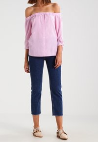 Růžovo-bílá pruhovaná halenka se stojáčkem a zapínáním na knoflíky, doplněná o zkrácené tmavě modré džíny a béžové boty na šněrování.