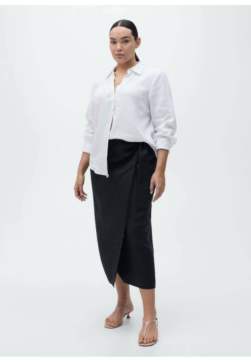 Chemise blanche en lin à boutons, jupe portefeuille noire avec une fente latérale, et sandales avec lanières. Accent sur le design minimaliste et les tissus contrastés.