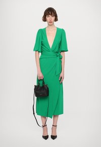 Green wrap dress with short puff sleeves and a deep V-neck, paired with a small black handbag and black high-heeled shoes.