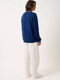 Marineblauwe gebreide trui met een ronde halslijn en lange mouwen, gecombineerd met losse witte denim broek en witte sneakers.