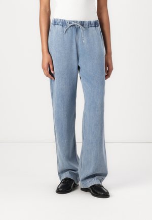 Persona que lleva pantalones vaqueros anchos de pierna en azul claro con cintura elástica y cordón, combinados con mocasines negros.