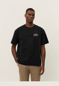 Tricou din bumbac negru cu mâneci scurte și decolteu rotund, având un mic logo auriu pe partea stângă a pieptului. Croială casual.