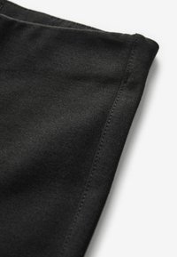 Černá tkanina s hladkým povrchem, s pečlivě přišitým okrajem. Materiál vypadá lehce a flexibilně.