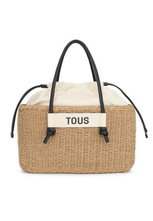 Sac en paille tressée avec un dessus à cordon en tissu crème, des accents en cuir noir et une étiquette beige bien en vue portant la mention "TOUS."