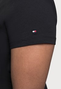 Sort bomulds t-shirt med korte ærmer, der har et lille rødt, hvidt og blåt logo på venstre ærme. Glat tekstur og tæt pasform.