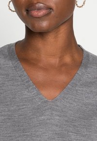Pull en V gris en maille avec une texture côtelée et une finition douce, présentant un gros plan du col et de la zone du cou.