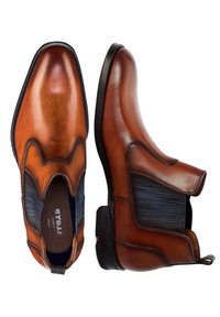 Ruskea nahkainen nilkkabootsit, joissa on joustavat sivupaneelit, teräväkärkiset ja sileäksi viimeistelty pinta. Varustettu kestävästä kumipohjasta ja huomaamattomista ommeltyksistä.