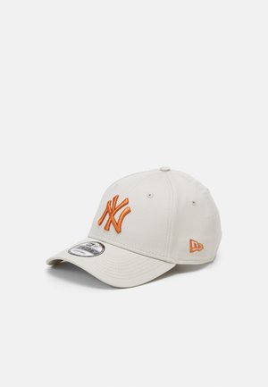Lysebeige baseballkasket med orange New York Yankees-logo foran og New Era-emblem på siden, buet skygge, på hvid baggrund.