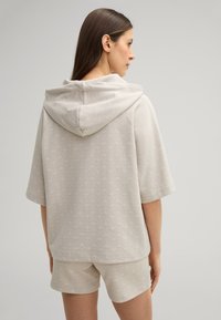 Lichtgrijze hoodie met een capuchon, korte mouwen en een subtiel patroon, in combinatie met bijpassende shorts. Zachte stoftextuur en een ontspannen pasvorm.