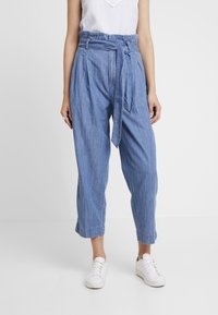 Světle modré široké kalhoty z denimové látky, s vysokým pasem a páskem na zavázání, mají volný střih a zkrácenou délku.