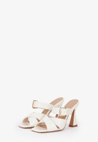 Witte leren hoge hakken sandalen met een open teen, met een gekruist bandontwerp en een gouden gespaccent op de enkelband.
