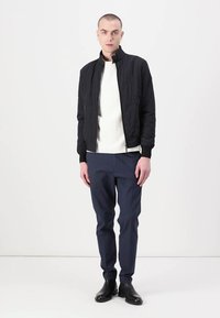Zwarte gewatteerde bomberjack, witte gestructureerde trui, marineblauwe broek en zwarte enkelboots. Slim fit met ribgebreide manchetten en zoom.