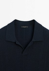 Polo en maille bleu marine à manches courtes avec rayures verticales texturées et col détente, posé à plat sur un fond blanc.