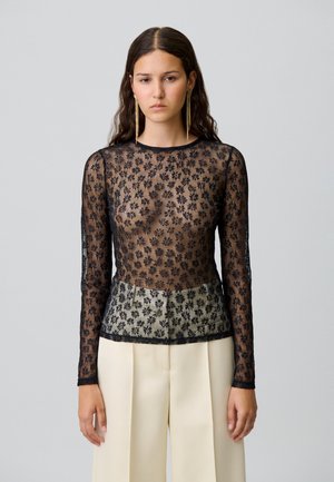 Top noir en dentelle florale à manches longues avec un corps semi-transparent et un ourlet uni à motifs. Associé à un pantalon ajusté de couleur claire.