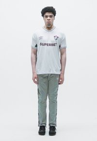 Conjunto atlético com uma camisola cinza claro com detalhes escuros e o logótipo "SUPERBET", combinado com calças de treino cinzas com riscas laterais.