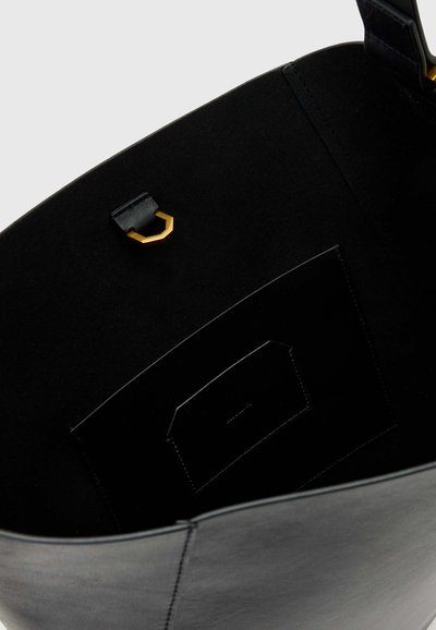Intérieur d'un sac en cuir noir montrant une petite poche intérieure et un anneau métallique en D doré fixé à une sangle en cuir.