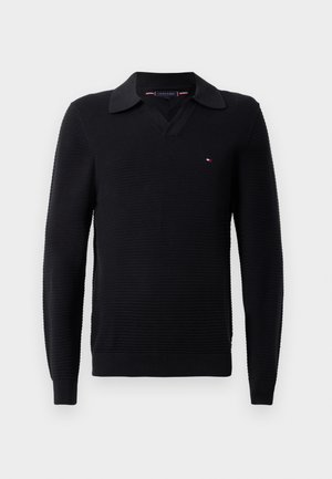 Črn pulover s teksturiranim pletenjem, z V-izrezom in kontrastnim ovratnikom. Majhna logotipna oznaka na prsih.