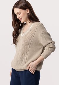 Maglione beige a V con un mix di texture a maglia e un pannello laterale in tessuto aperto; polsini e orlo ribattuti aggiungono dettagli.