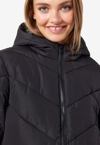 Veste en duvet matelassée noire avec capuche, présentant une fermeture éclair à l'avant, une couture en chevrons et une texture lisse et légère.