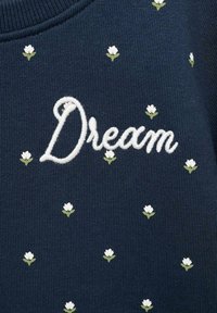 Felpa navy con testo ricamato in bianco "Dream" e motivi floreali bianchi sparsi con steli verdi. Tessuto a coste testurizzato.