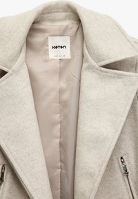 Cappotto grigio chiaro, strutturato, con ampio colletto, due tasche con zip e una morbida fodera interna in satin. Etichetta visibile all'interno.