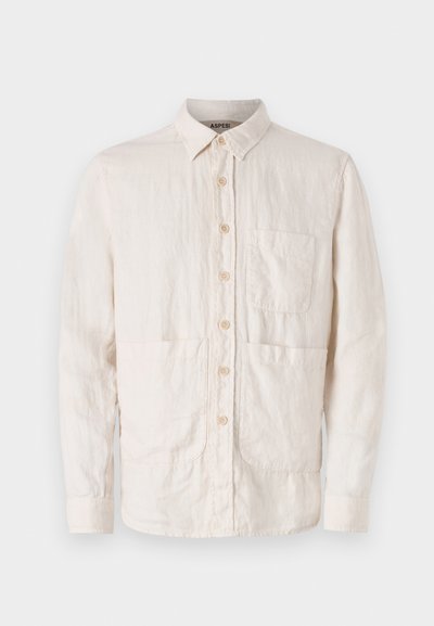 Lysbeige skjorte med knapper lavet af tekstureret stof. Har en krave, syv forreste knapper og to forreste stiklommer.