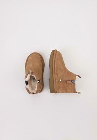 Botas de tobillo de ante marrón con forro de pelaje sintético, cierre con cremallera lateral y suela de goma, con costuras en contraste y una lengüeta.
