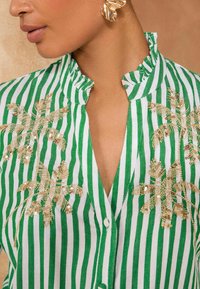 Camicia a righe verdi e bianche con colletto alla coreana, decorata con ricami di palme in paillettes dorate sul davanti.